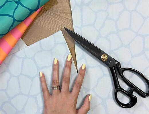 mãos que vão cortar papel tecidos coloridos com uma tesoura, simbolizando a ideia de recomeçar e criatividade.